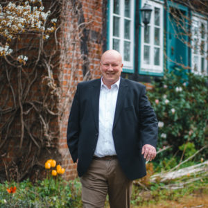 Felix Gieske-Wollerich steht vor einem alten Fachwerkhaus. Er trägt ein weißes Hemd und darüber ein schwarzes Sakko.