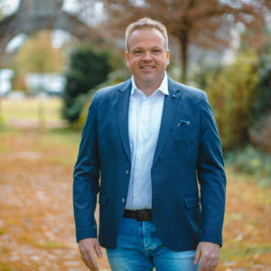 Chrsitian steht vor einem Tor. Im Hintergrung ist grüne Landschaft zu sehen.